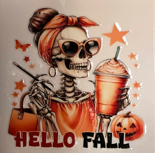 Skeleton holding a pumpkin spice latte with 'Hello Fall' text on a decorative card.