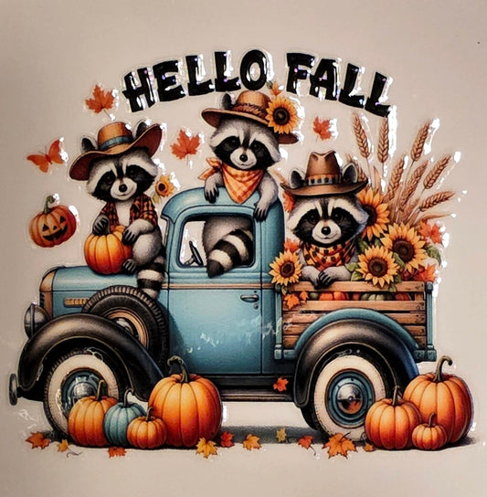 Decorative sign with raccoons in a truck and 'Hello Fall' text on a marble surface.